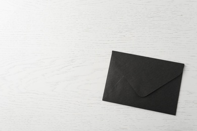Photo of Black paper envelope on white wooden background, top view. Space for text
