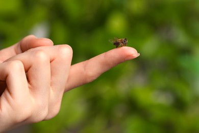 Photo of Bee going to sting woman on green blurred background, closeup. Space for text