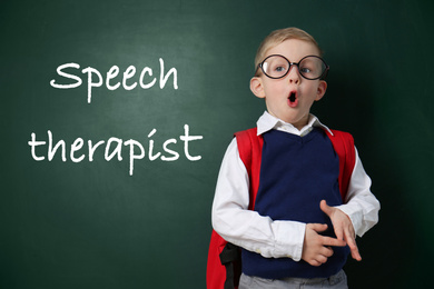 Cute little child near chalkboard and text Speech Therapist 