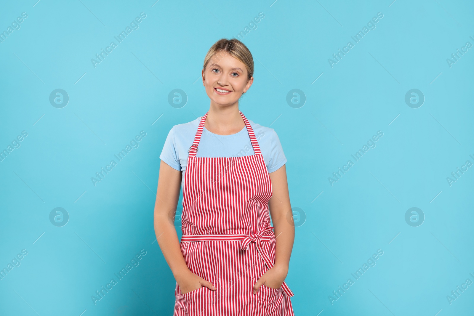 Photo of Beautiful young woman in clean striped apron on light blue background