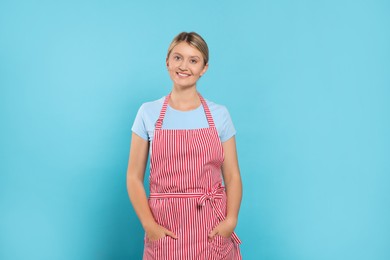 Photo of Beautiful young woman in clean striped apron on light blue background