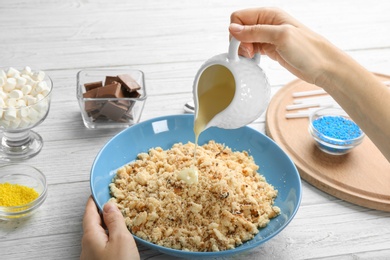 Photo of Woman making tasty cake pops at white wooden table, closeup