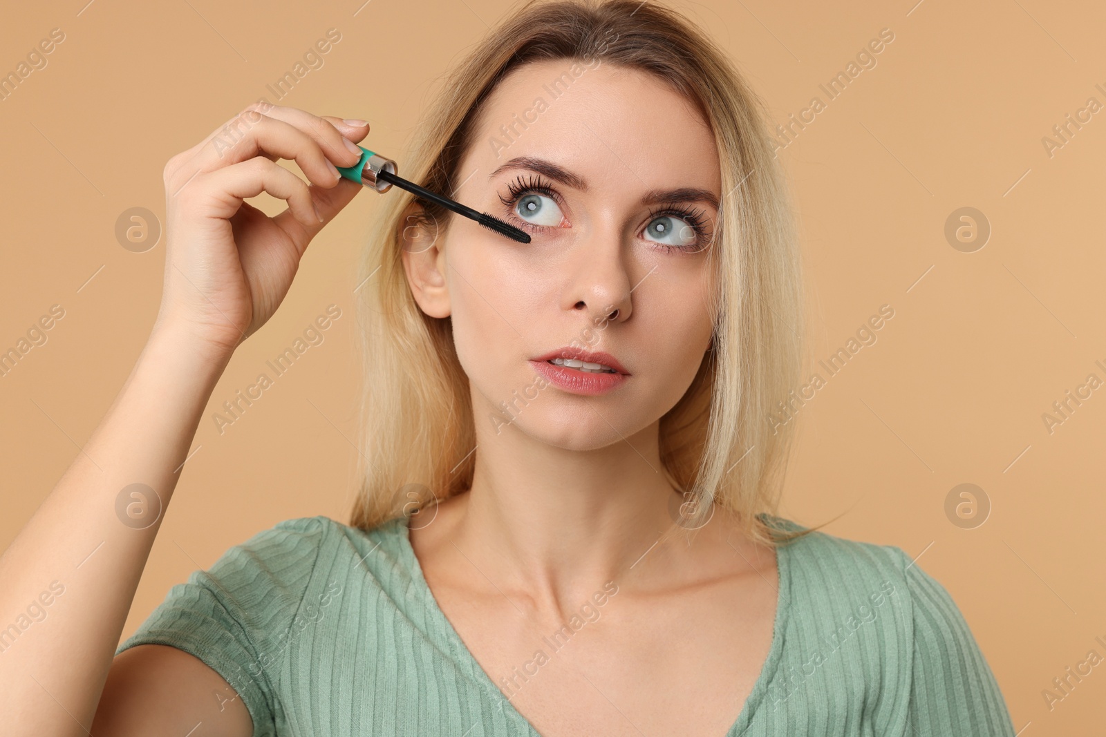 Photo of Beautiful woman applying mascara on beige background