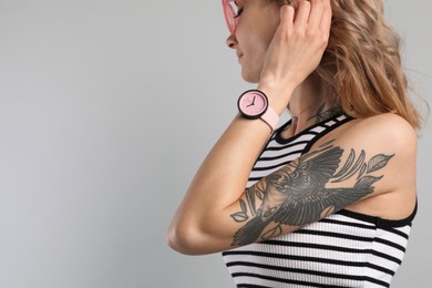Photo of Beautiful woman with tattoos on arm against grey background, closeup. Space for text