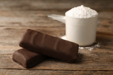 Photo of Tasty protein bars and scoop of powder on wooden table