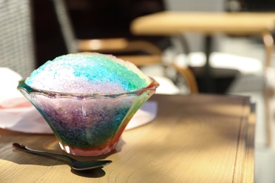 Photo of Rainbow shaving ice in glass dessert bowl and spoon on wooden table outdoors