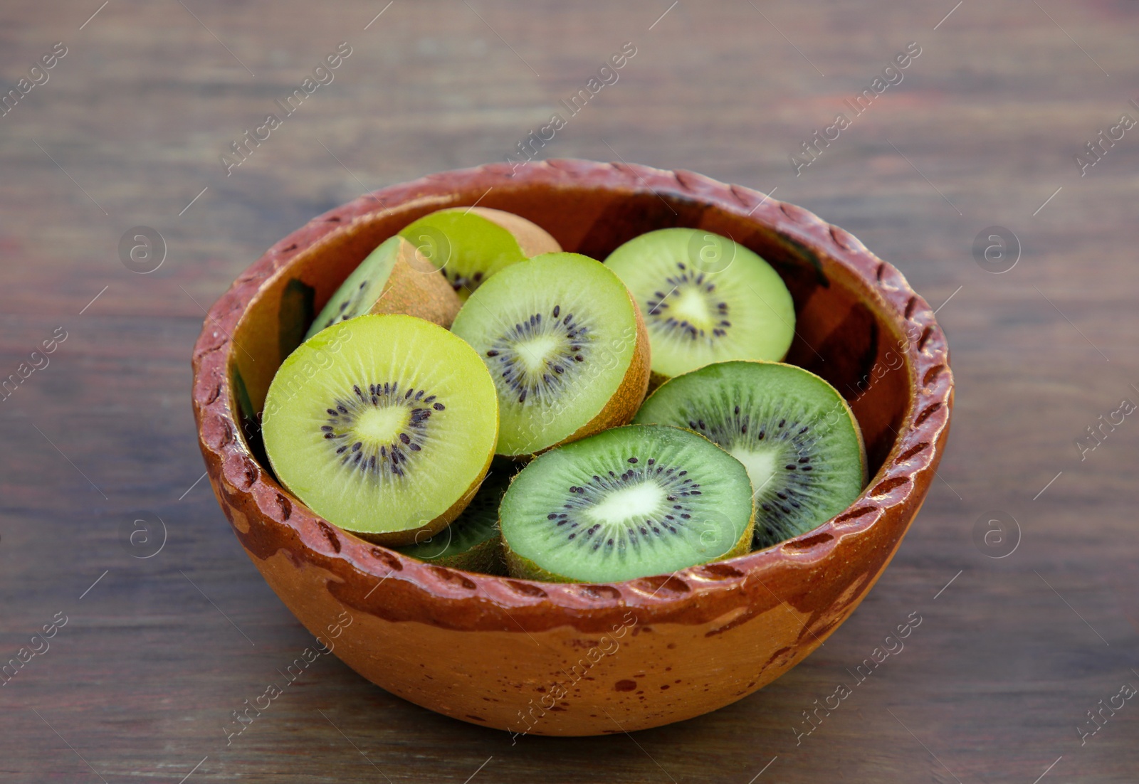 Photo of Bowl of many cut fresh kiwis on wooden table, closeup