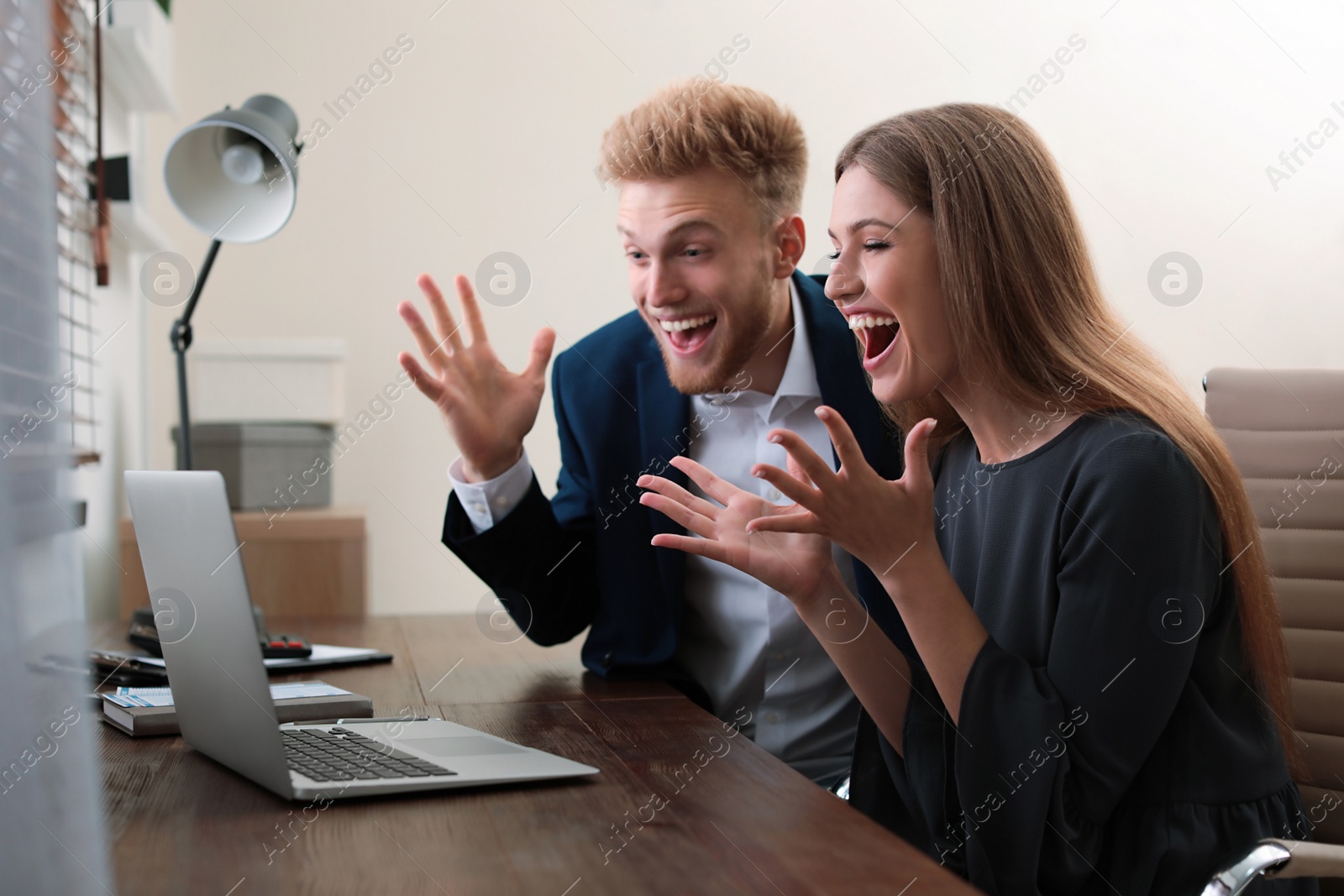 Photo of Happy young people playing online lottery using laptop at table in office