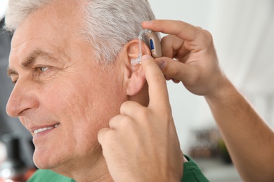 Photo of Young man putting hearing aid in father's ear indoors, closeup