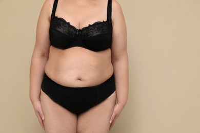 Beautiful overweight woman in black underwear on beige background, closeup with space for text. Plus-size model