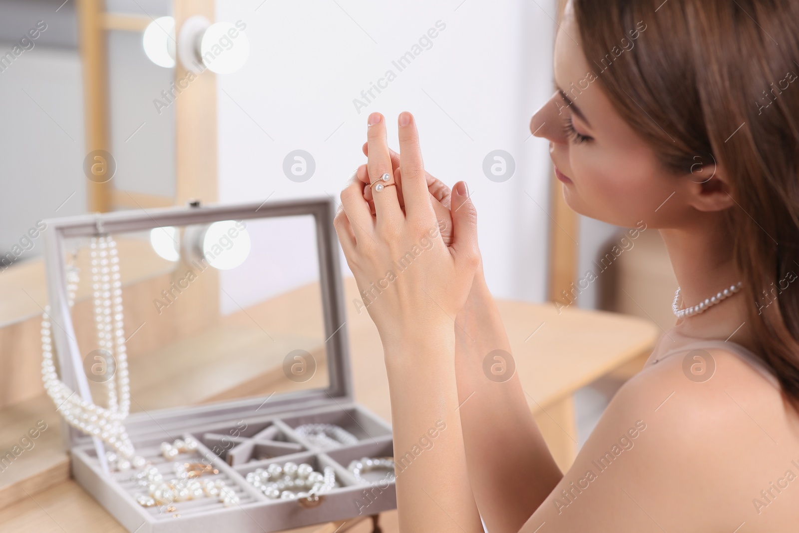 Photo of Young woman trying on elegant ring with pearls indoors, closeup. Space for text