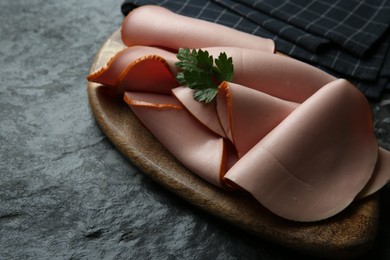 Photo of Board with slices of tasty boiled sausage and parsley on dark textured table, closeup