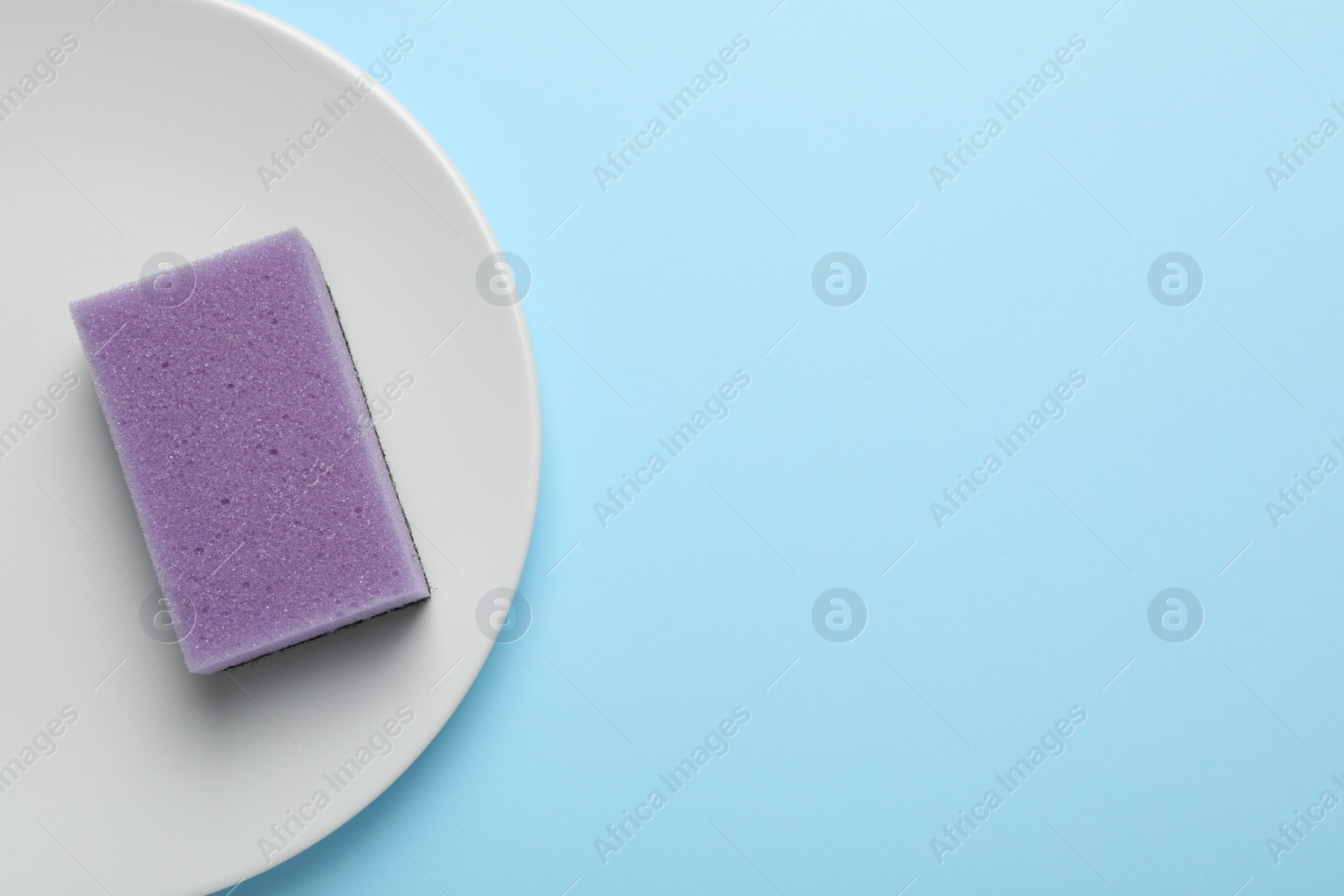 Photo of Plate with sponge on light blue background, top view. Space for text