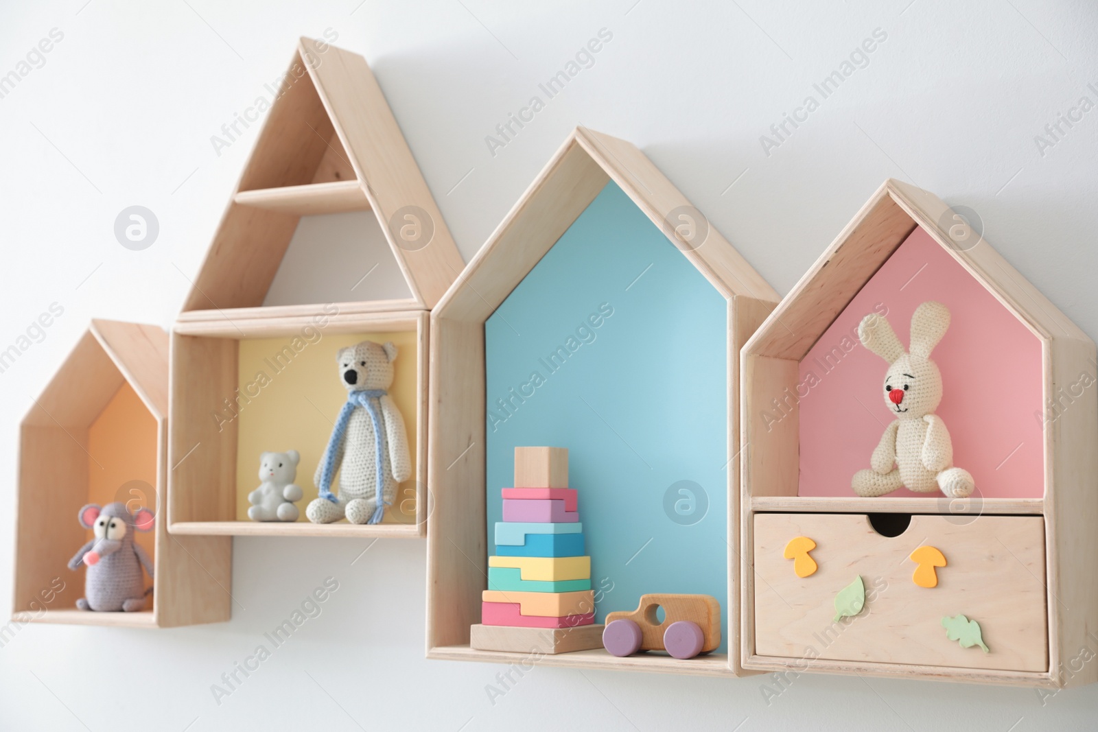 Photo of Different house shaped shelves with toys on white wall. Interior design