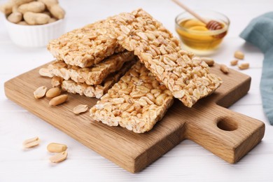 Photo of Board with tasty kozinaki bars, peanuts and honey on white wooden table