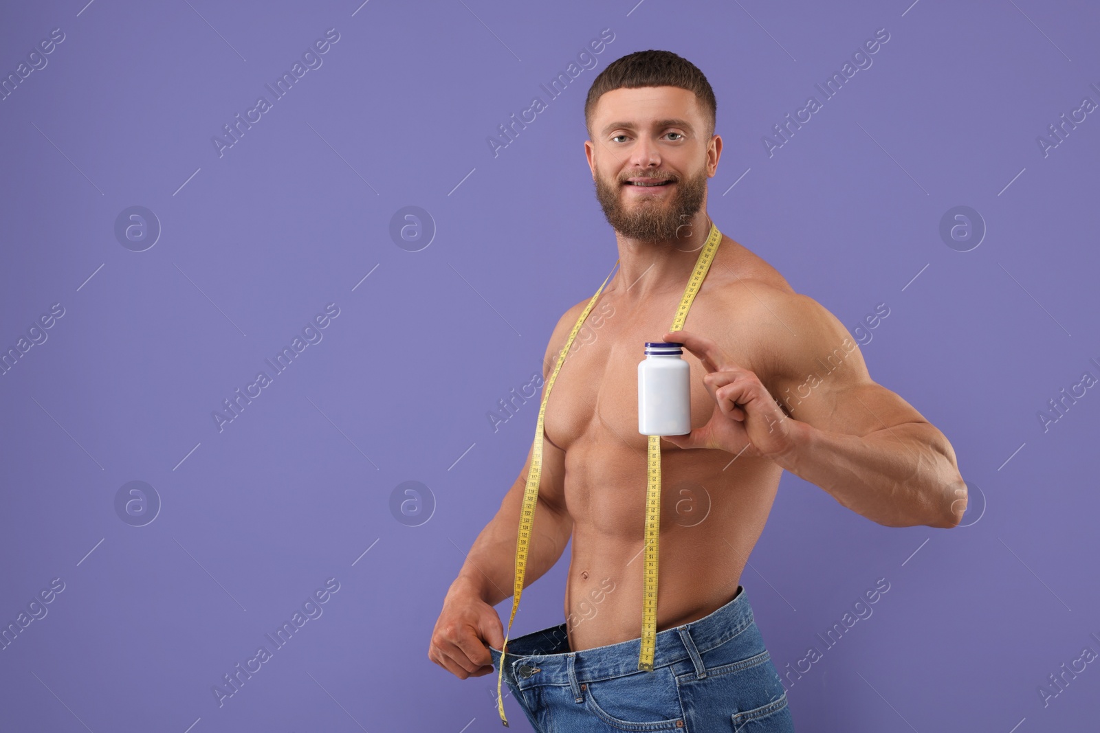 Photo of Athletic young man with measuring tape and bottle of supplements wearing big jeans on purple background, space for text. Weight loss