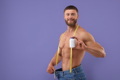 Athletic young man with measuring tape and bottle of supplements wearing big jeans on purple background, space for text. Weight loss