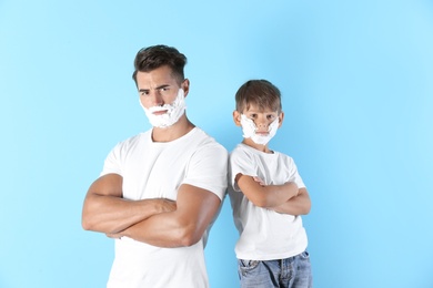 Photo of Father and son with shaving foam on faces against color background
