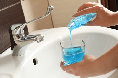 Photo of Woman pouring mouthwash from bottle into glass in bathroom, closeup. Teeth care