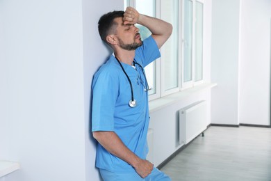 Photo of Exhausted doctor near white wall in hospital hallway