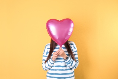 Young woman with heart shaped balloon on color background