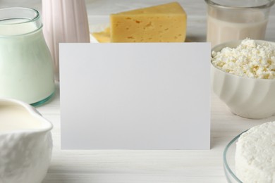 Dairy products and blank card on white wooden table, closeup. Space for text