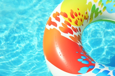 Colorful inflatable ring floating in swimming pool on sunny day. Space for text