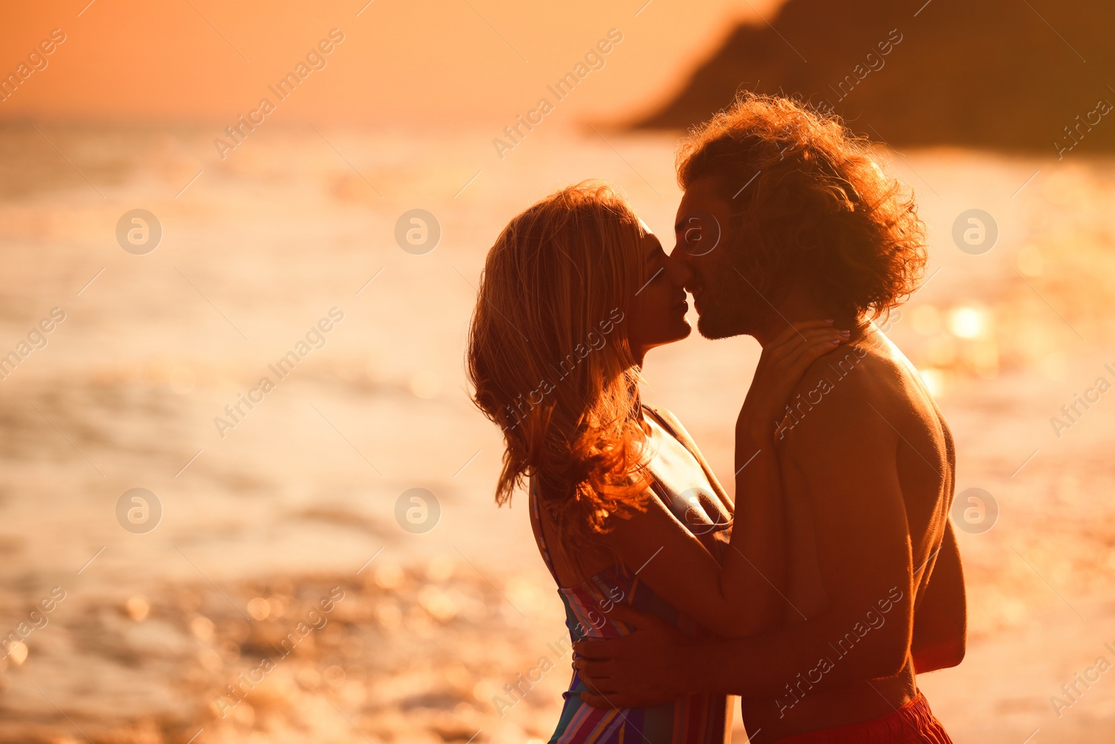 Photo of Young woman in bikini kissing her boyfriend on beach at sunset. Lovely couple