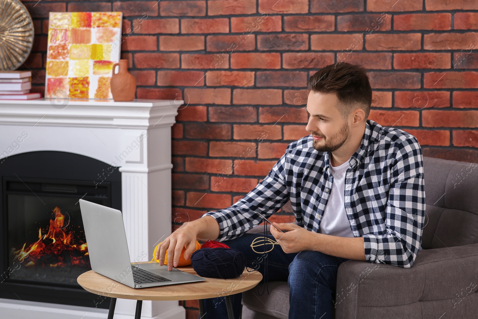 Photo of Man learning to knit while watching online course on laptop at home. Time for hobby