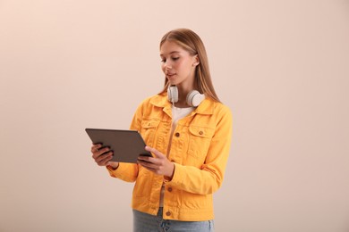 Photo of Teenage student with tablet and headphones on beige background