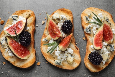 Photo of Bruschettas with cheese, figs and blackberries on grey table, top view