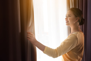 Image of Woman opening window curtains at home in morning