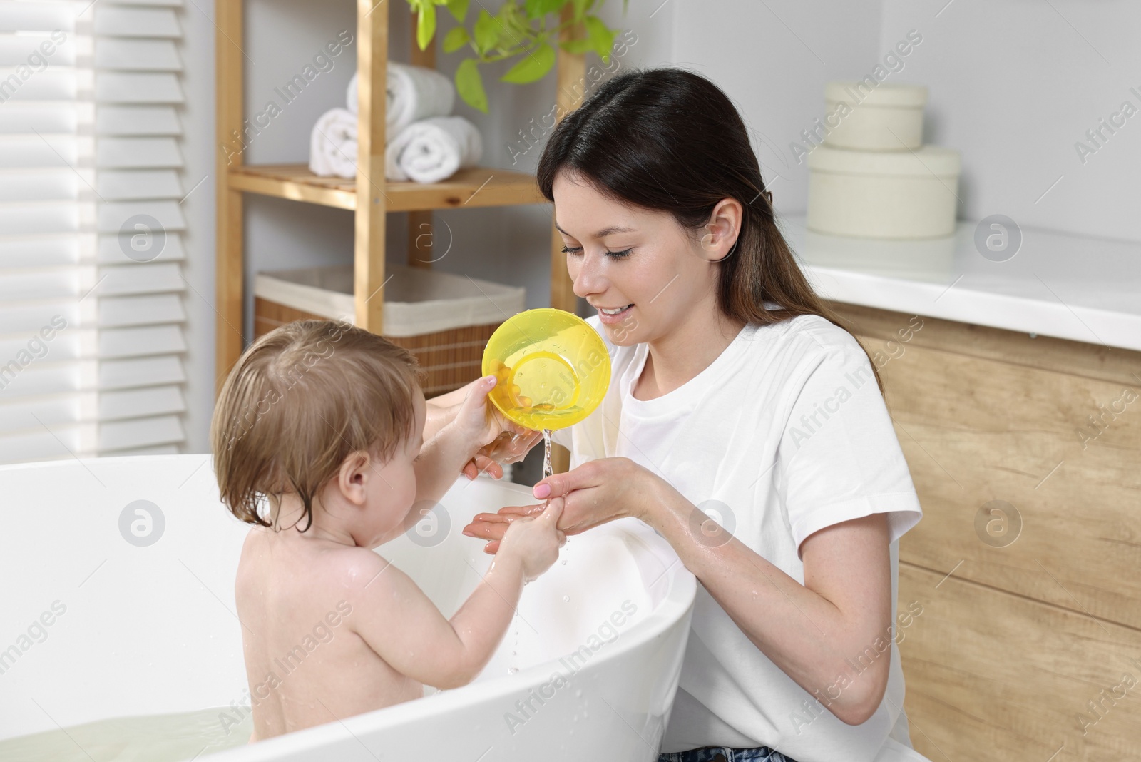 Photo of Mother bathing her cute little baby in tub at home