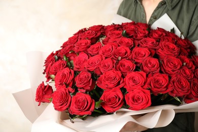 Photo of Woman holding luxury bouquet of fresh red roses on light background, closeup