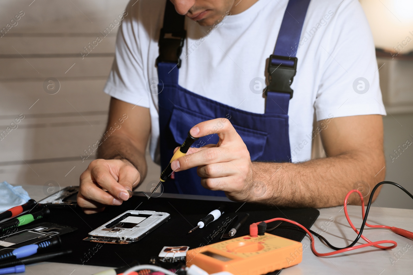Photo of Technician repairing broken smartphone at table indoors, closeup