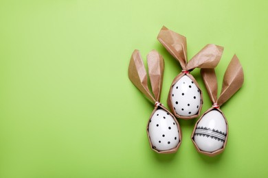 Easter bunnies made of craft paper and eggs on light green background, flat lay. Space for text