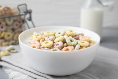 Photo of Tasty colorful cereal rings and milk in bowl on table, closeup