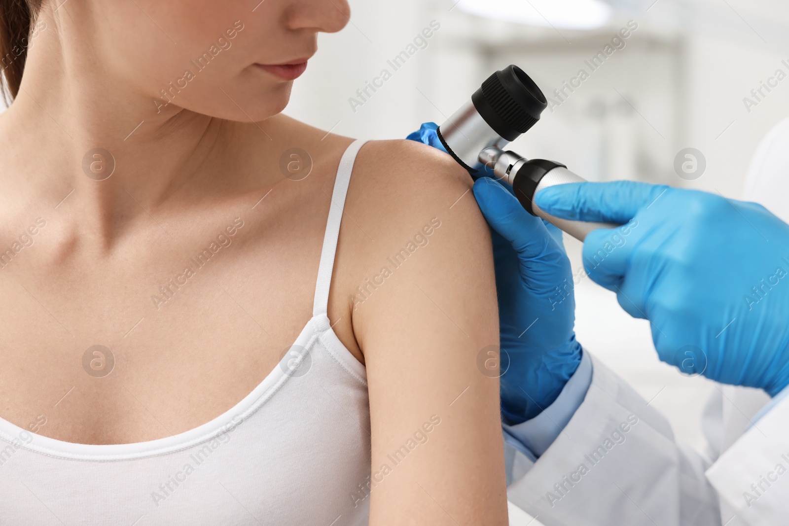 Photo of Dermatologist with dermatoscope examining patient in clinic, closeup