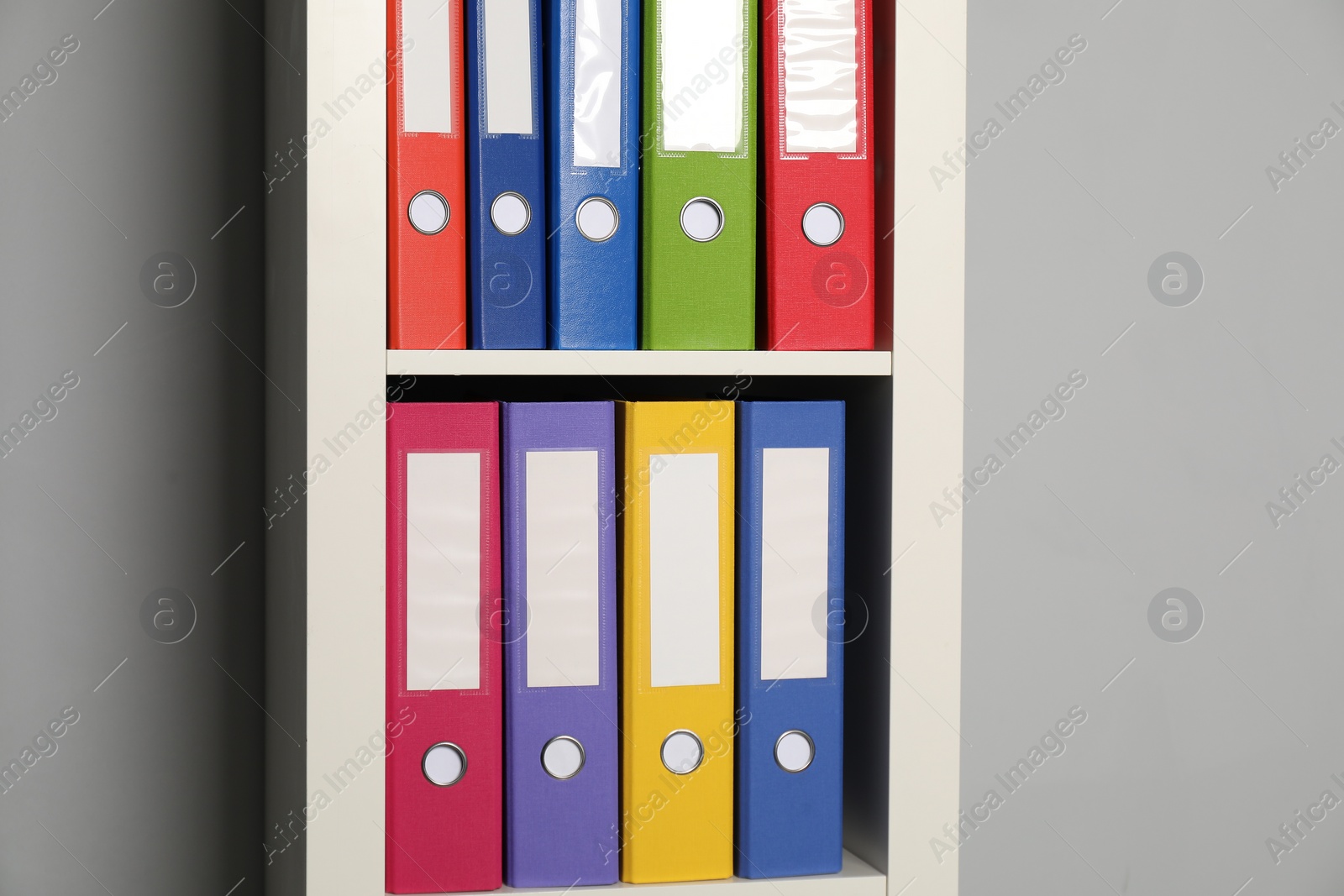 Photo of Colorful binder office folders on shelving unit near light grey wall