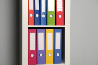 Photo of Colorful binder office folders on shelving unit near light grey wall