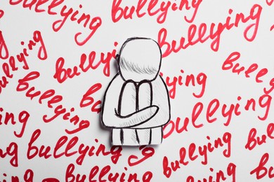 Photo of Child paper figure and words Bullying written on white background, top view