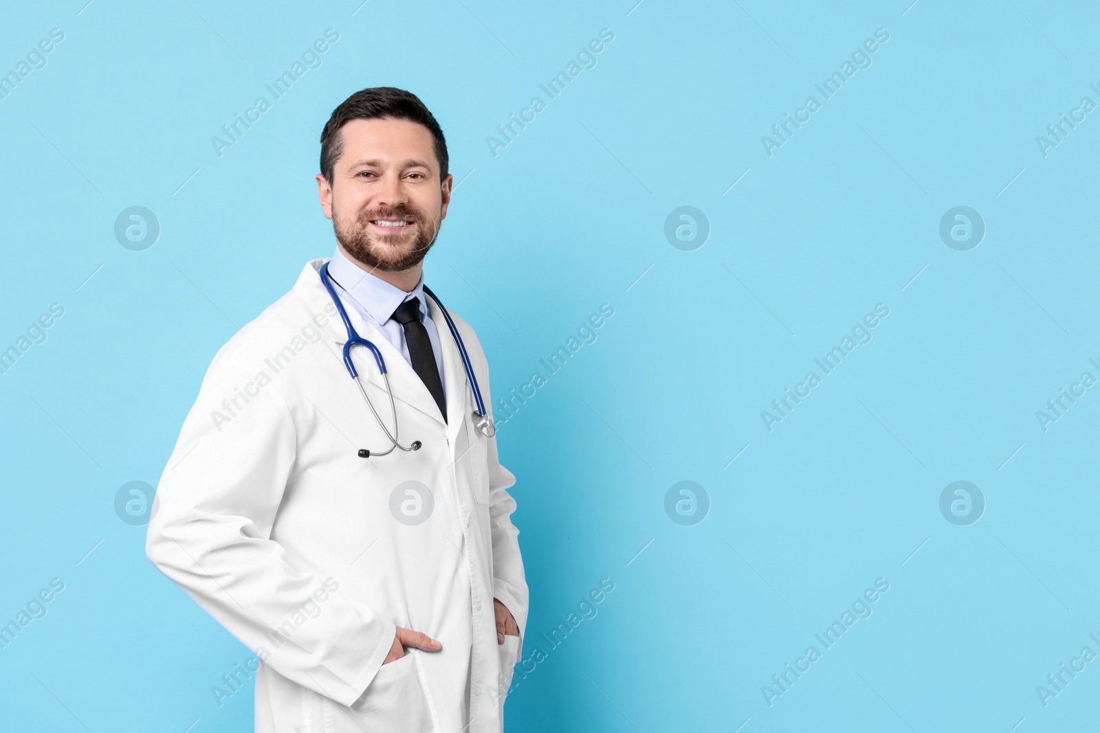 Photo of Smiling doctor with stethoscope on light blue background. Space for text