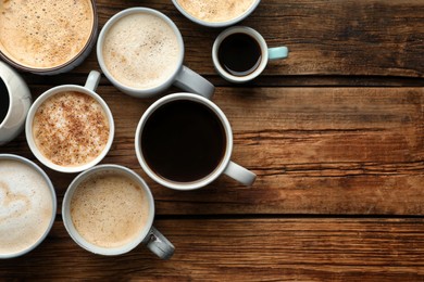 Many cups of different coffees on wooden table, flat lay. Space for text