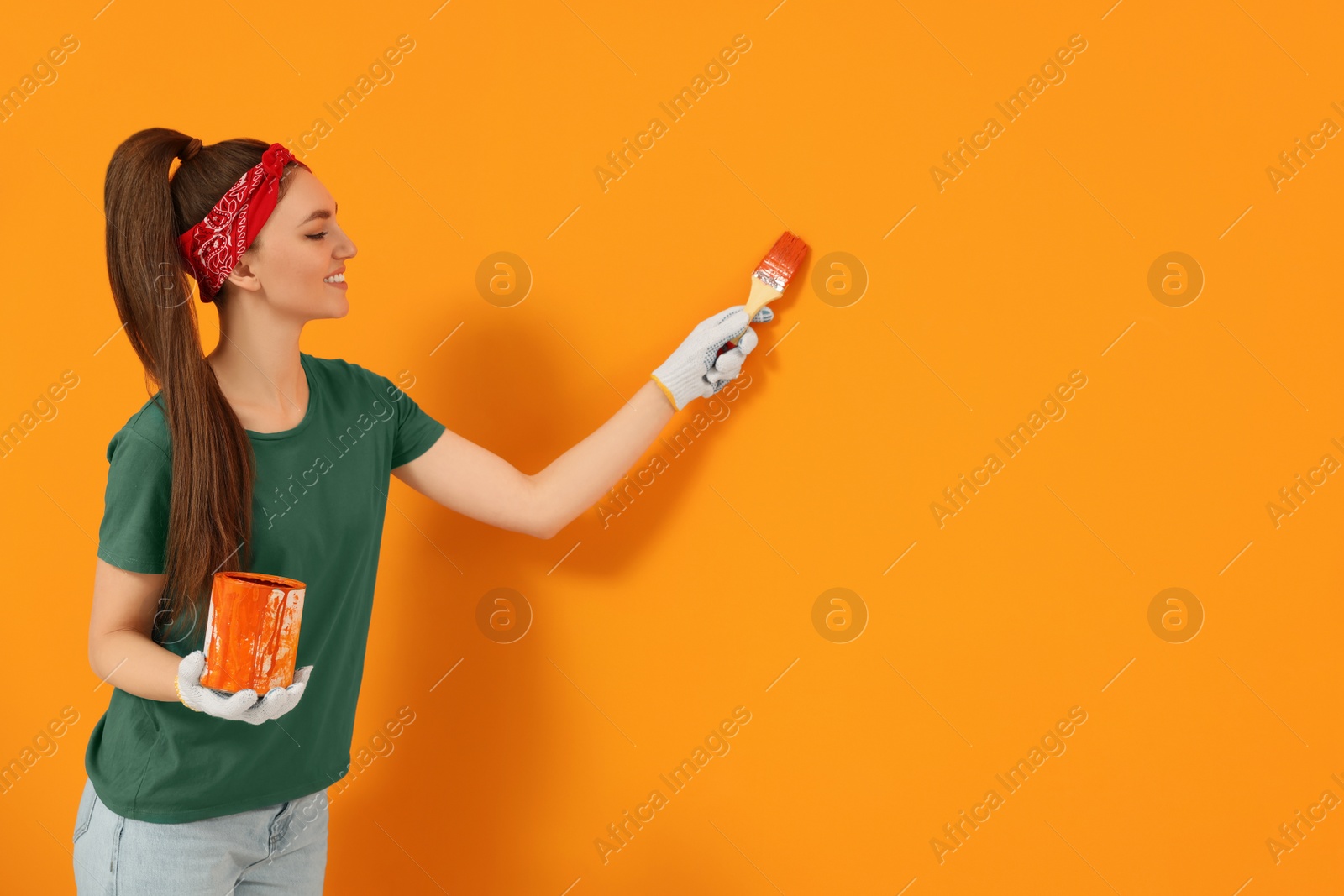 Photo of Designer painting orange wall with brush, space for text