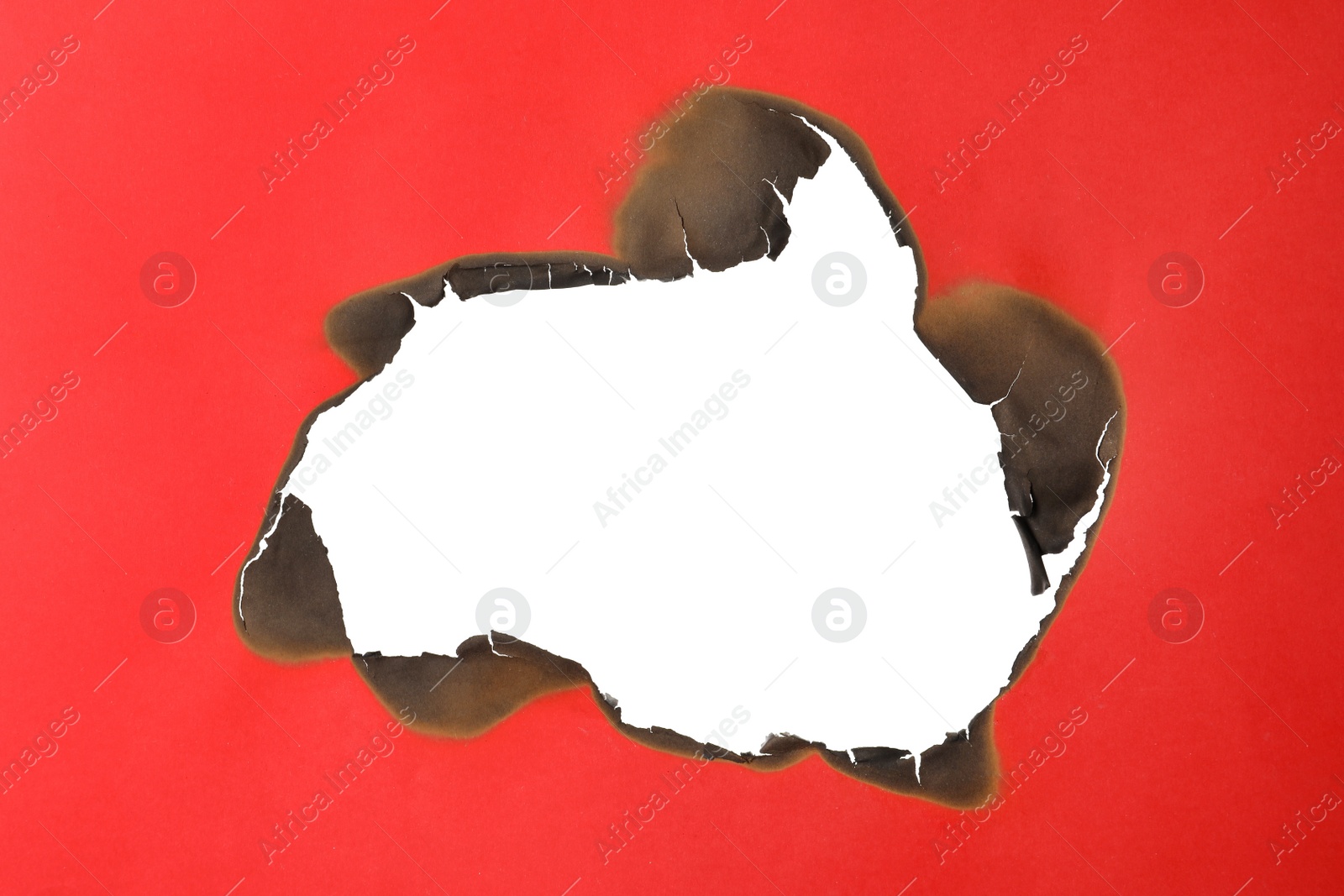 Photo of Burnt hole in red paper on white background, space for text