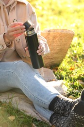 Photo of Picnic time. Woman opening thermos on green grass outdoors, closeup