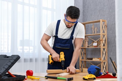 Young worker using electric drill at table in workshop