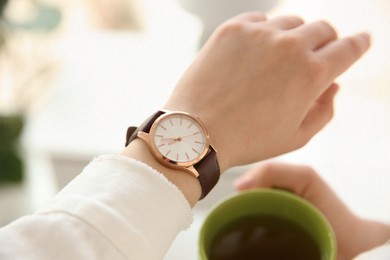 Woman with luxury wristwatch and cup of tea on blurred background, closeup