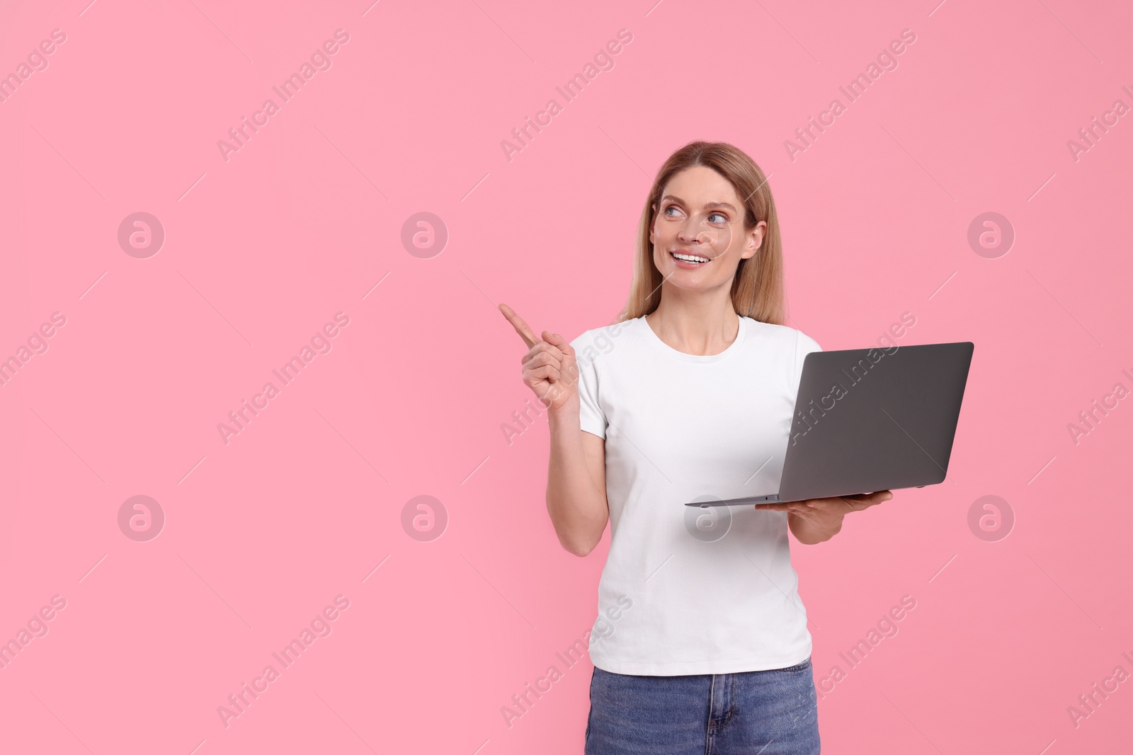 Photo of Happy woman with laptop pointing at something on pink background. Space for text