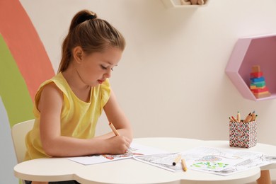 Photo of Little girl coloring antistress page at table indoors